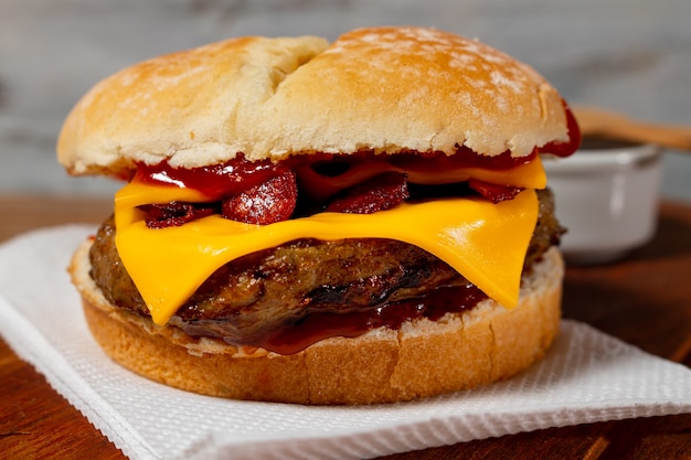 Delicioso hambúrguer com bacon e queijo cheddar no pão caseiro com sementes e ketchup sobre uma superfície de madeira e fundo rústico.