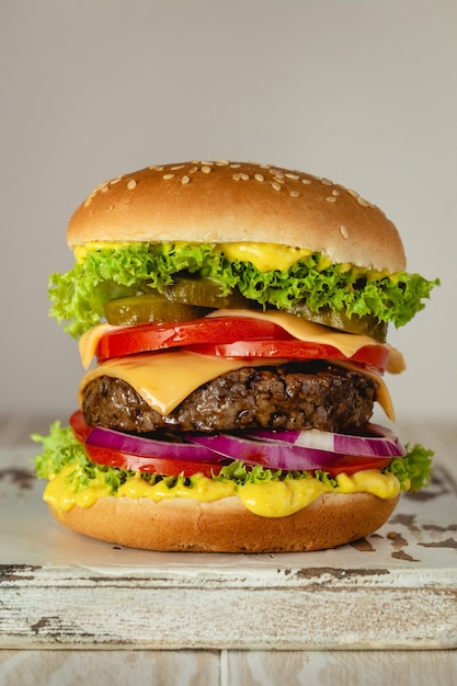 Delicioso hambúrguer com carne, queijo derretido, molho pingando e legumes em fundo branco rústico. Hambúrguer saboroso feito na hora, close-up