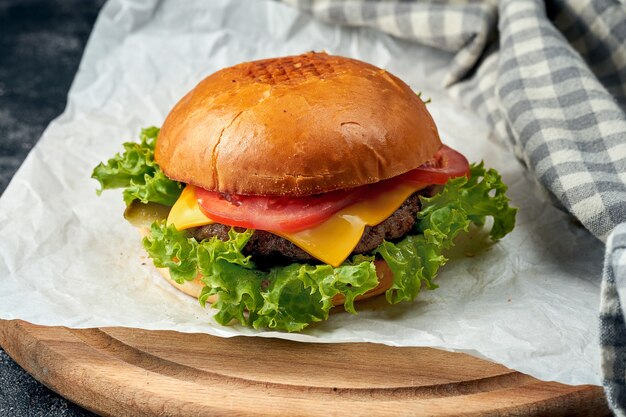 Delicioso hambúrguer com carne, tomate, alface, queijo derretido em pergaminho branco. superfície escura. fast food americano