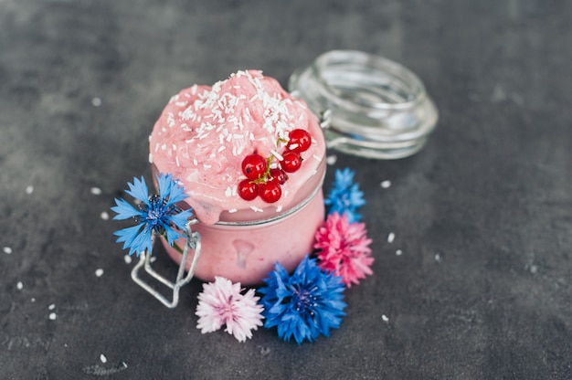 Delicioso helado de fresa decorado con hojuelas de coco, grosellas rojas y acianos azules sobre fondo gris. Sabroso postre. Concepto de comida