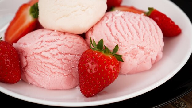 Delicioso helado de fresa con fresas frescas en un plato blanco y negro. Sabroso postre frío de verano.