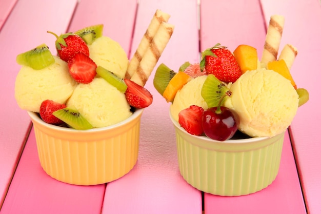 Delicioso helado con frutas y bayas en un tazón sobre mesa de madera