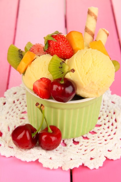 Delicioso helado con frutas y bayas en un tazón sobre mesa de madera