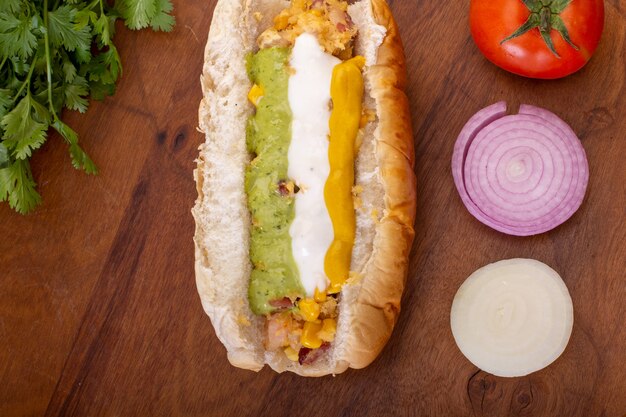 Delicioso hot dog con ingredientes y sobre fondo de madera o colores