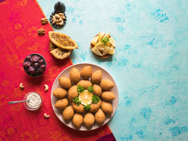 Foto delicioso kibbeh frito con salsa de yogurt en un recipiente servido en un plato sobre una mesa azul. receta clásica libanesa.