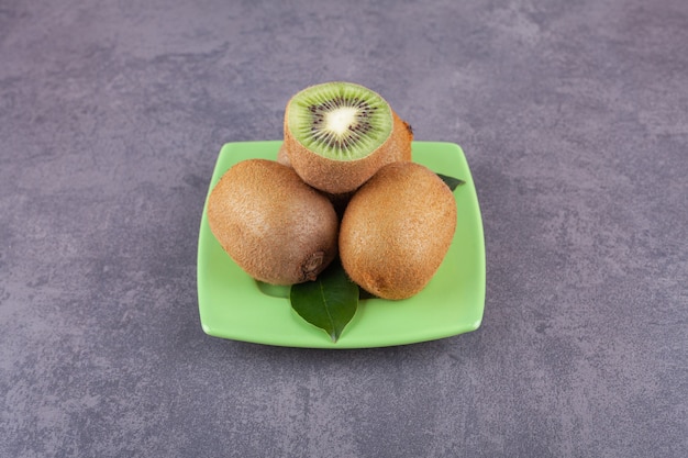 Delicioso kiwi entero y en rodajas con hojas colocadas sobre una placa verde.