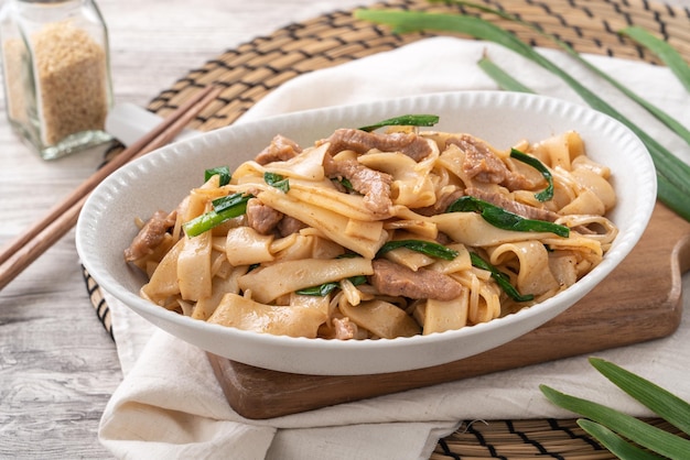 Delicioso macarrão de arroz liso taiwanês taiwanês com carne de porco fatiada e legumes em uma tigela sobre fundo branco