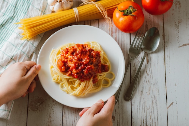 Delicioso macarrão espaguete caseiro com molho de tomate e carne picada servido em um prato branco com ingredientes em uma superfície de madeira branca