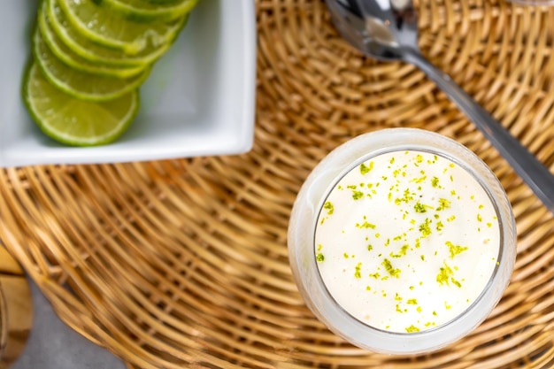 Delicioso mousse de limón en un plato de paja y un fondo de mesa blanco con limones enteros y en rodajas en el fondo y una cuchara de metal