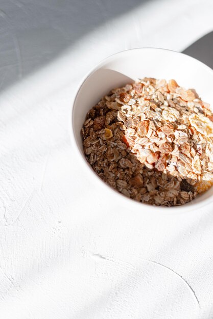 Delicioso muesli de desayuno crudo en pensamiento blanco sobre mesa blanca temprano en la mañana al amanecer