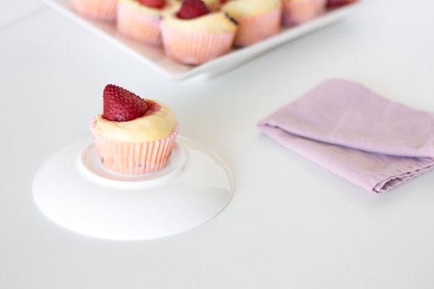 Delicioso muffin de fresa en un plato blanco con una fresa recién cortada en el lateral.