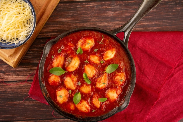 Delicioso nhoque com molho de tomate vermelho e manjericão servido em uma frigideira preta em um fundo de madeira na vista superior