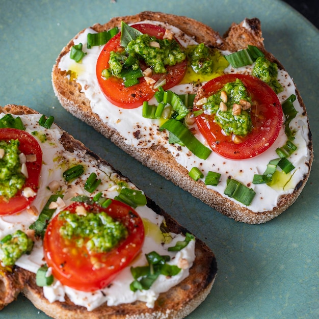 Delicioso pan tostado con queso crema blanco, ajo silvestre verde y tomate en el plato de cerca