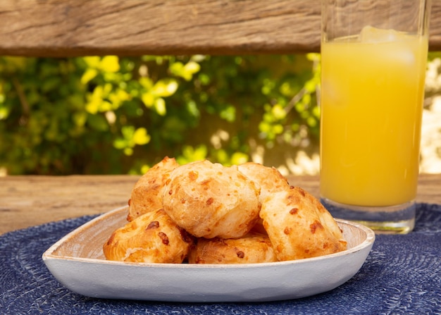 Delicioso pão de queijo Minas em uma bancada de madeira rústica ao ar livre com um copo de suco de laranja