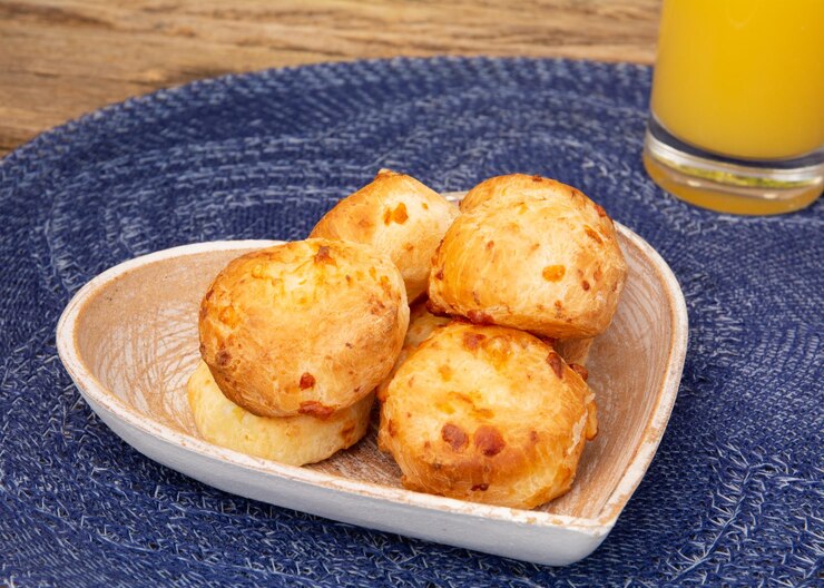 Foto delicioso pão de queijo minas em uma bancada de madeira rústica ao ar livre com um copo de suco de laranja
