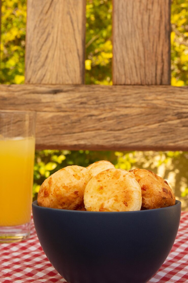 Foto delicioso pão de queijo minas em uma bancada de madeira rústica ao ar livre com um copo de suco de laranja