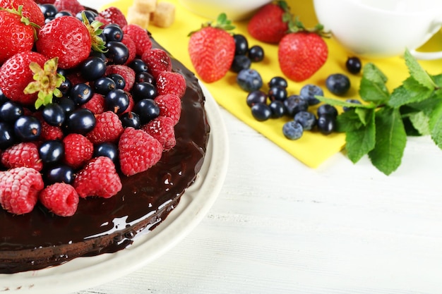 Delicioso pastel de chocolate con bayas de verano sobre un fondo blanco de madera