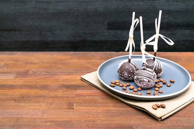 Delicioso pastel de chocolate dulce, paletas heladas decoradas con chispitas blancas en un plato de fondo de madera postres de pastelería en un palo con cinta Comida sabrosa maqueta espacio de copia de plantilla
