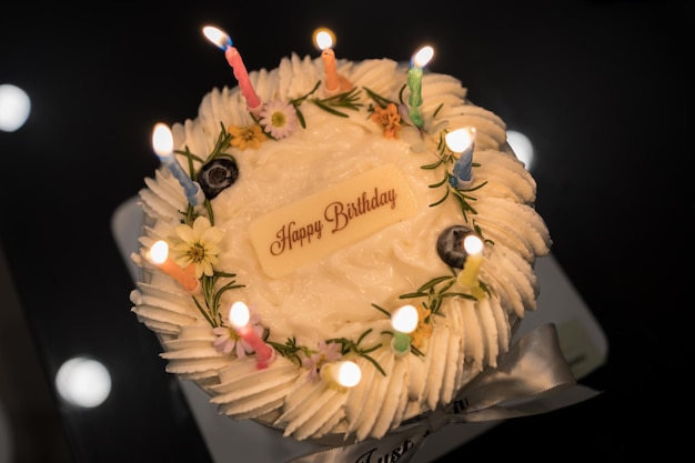 Delicioso pastel de coco de cumpleaños decorado con hermosas flores y velas sobre fondo negro texturizado