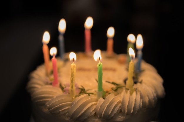 Delicioso pastel de coco de cumpleaños decorado con hermosas flores y velas sobre fondo negro texturizado