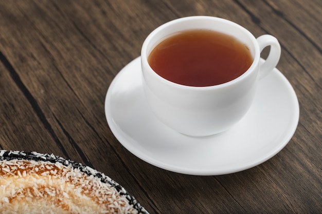 Delicioso pastel de coco y taza de té negro en la mesa de madera.