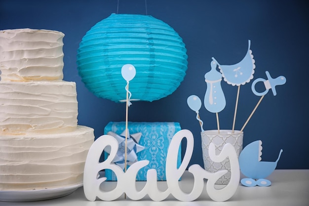 Foto delicioso pastel y decoraciones para fiesta de baby shower en la mesa cerca de la pared de color