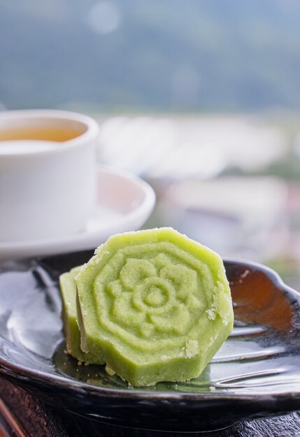 Delicioso pastel de frijol mungo verde con plato de té negro sobre la baranda de madera de una casa de té