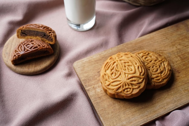 Delicioso pastel de luna tradicional completo y medio cortado con un relleno dulce y un vaso de leche.