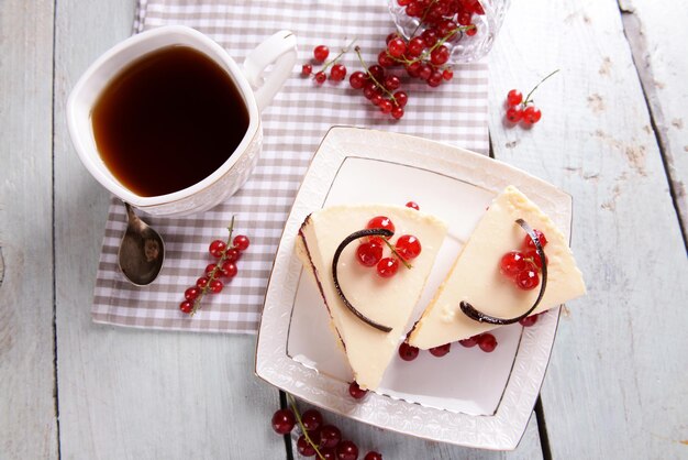 Delicioso pastel de queso con bayas y una taza de té en la mesa de cerca