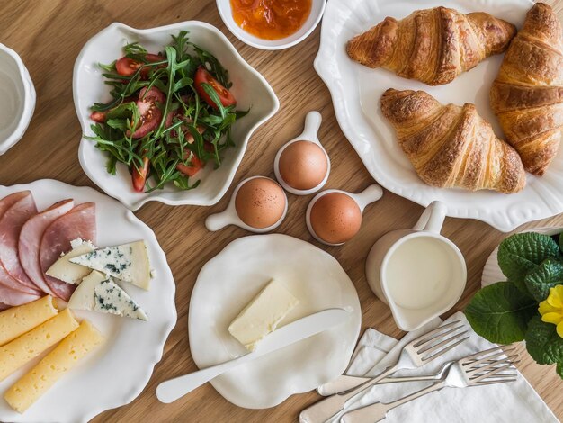 Delicioso pequeno-almoço variado brunch croissants ovos presunto queijo manteiga damasco salada de legumes frescos em uma mesa de madeira vista superior