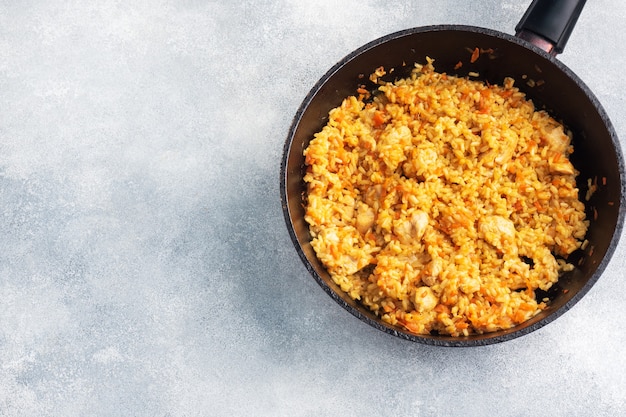 Delicioso pilaf asiático, arroz guisado con verduras y pollo en una sartén. hormigón gris. Copie el espacio.