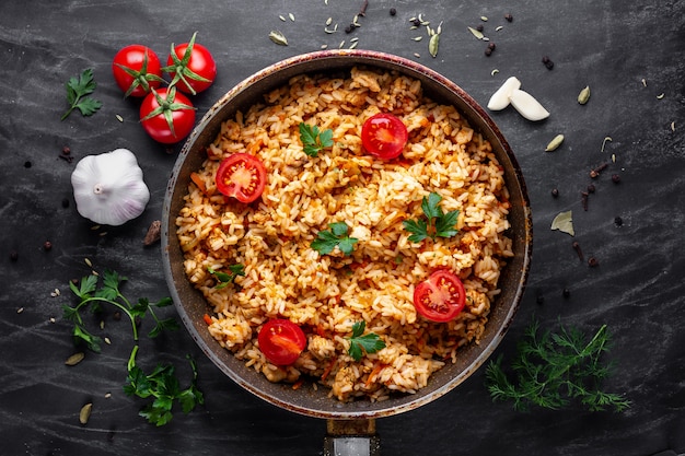 Delicioso pilaf casero con pollo, perejil fresco y verduras maduras en una sartén para almorzar en un surfce oscuro. Vista superior