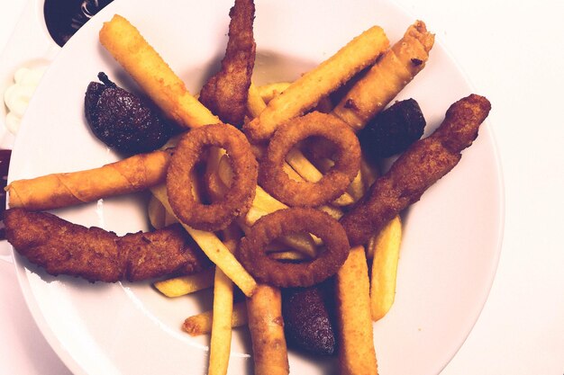 Delicioso plato de bocadillos papas fritas aros de cebolla rollitos de primavera o salchichas en la mesa