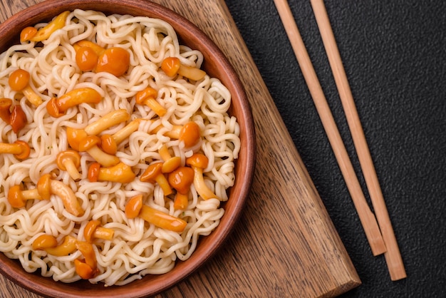 Delicioso plato de cocina asiática con fideos de arroz, pimientos, champiñones y especias sobre un fondo de hormigón oscuro