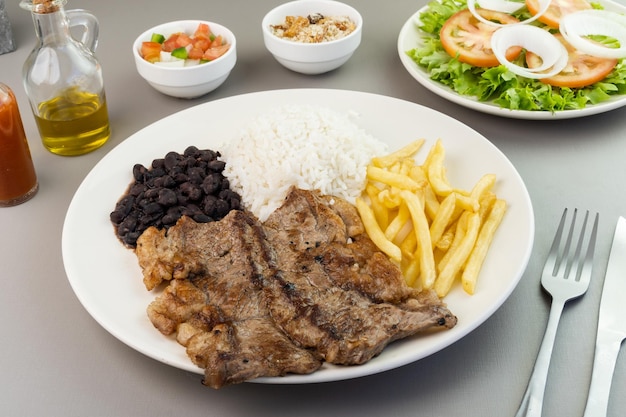 Delicioso plato ejecutivo de filete de res arroz frijoles papas fritas y ensalada verde con lechuga tomate y cebolla acompañado de farofa y vinagreta Comida típica brasileña Enfoque selectivo