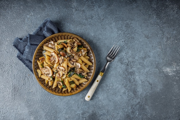 Delicioso plato italiano, pasta Penne con spanach, calabacín y champiñones asados con ajo en la mesa con textura de mármol azul. Pasta integral y champiñones enteros