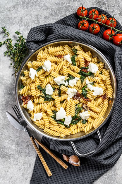 Delicioso plato de pasta fusilli con cremosa salsa de espinacas y tomates secos. Fondo gris Vista superior