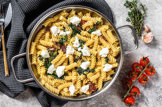 Delicioso plato de pasta fusilli con salsa cremosa de espinacas y tomates secos. Fondo gris. Vista superior.