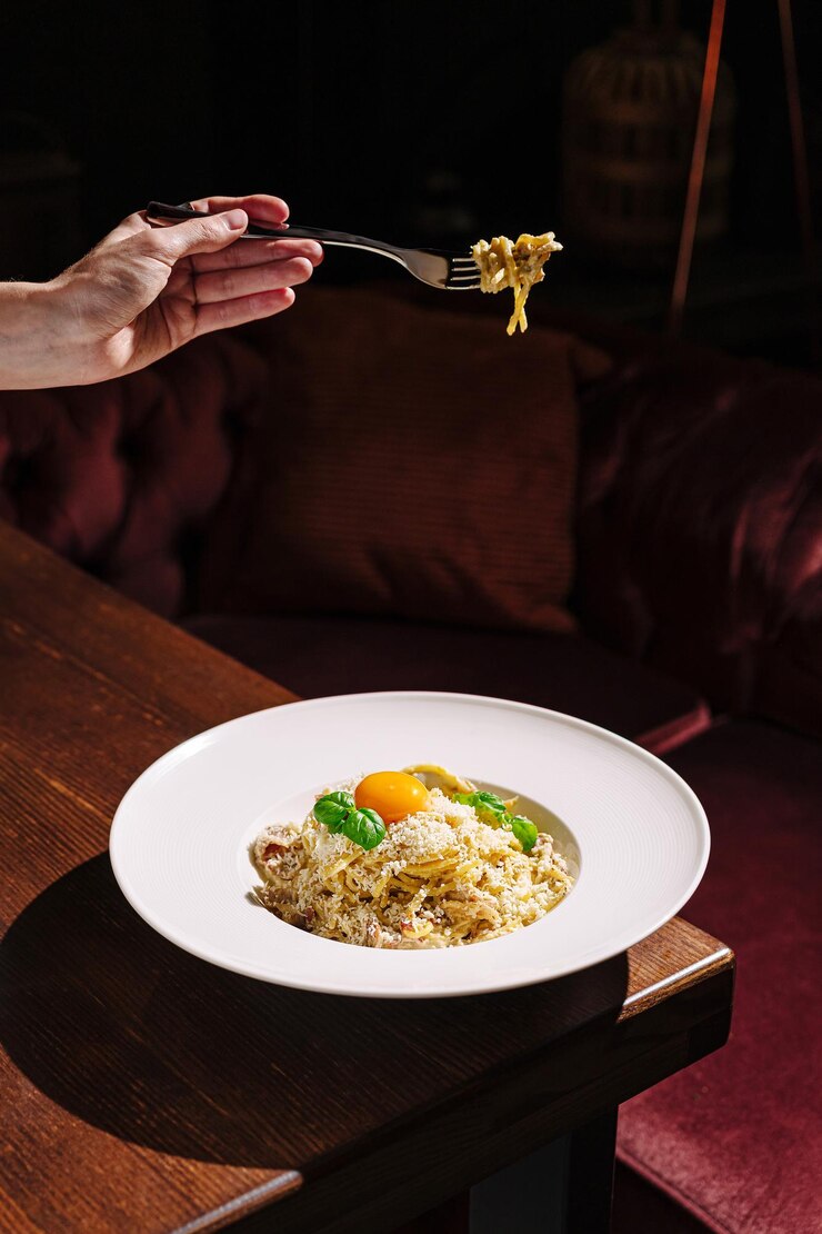 Un delicioso plato de pasta servido con ingredientes frescos y una vibrante yema de huevo en un restaurante de lujo