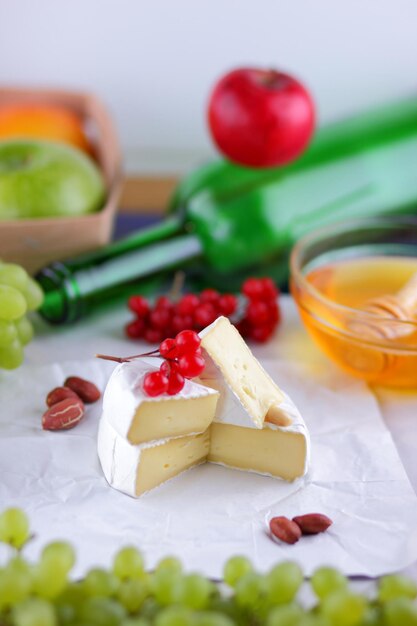 Delicioso plato saludable con frutas, nueces, miel, queso camembert sobre pergamino blanco Bodegón de queso, fruta y una botella verde sobre un fondo borroso Primer plano