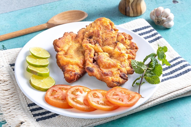 Delicioso pollo empanizado de pollo milanés con pan rallado y huevo, un plato típico brasileño En un plato blanco con tomates limón sobre un mantel blanco a rayas y mármol azul