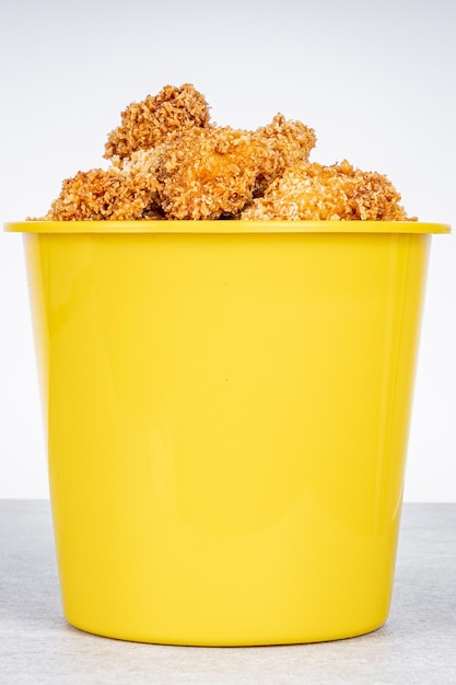 Foto delicioso pollo frito en un cubo amarillo sobre un fondo de mármol