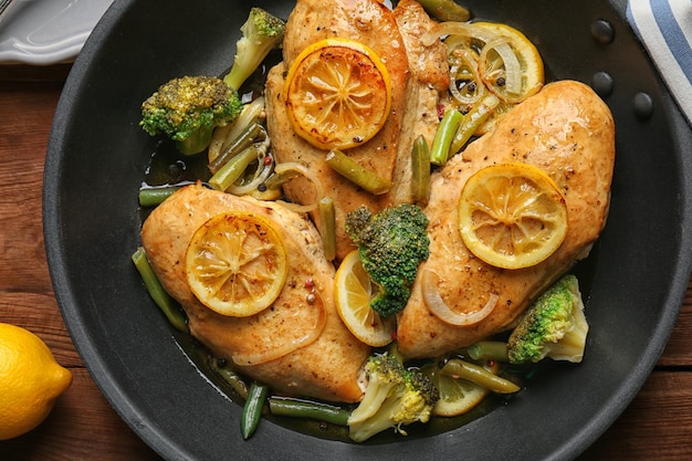 Delicioso pollo con limón y verduras en sartén sobre mesa de madera