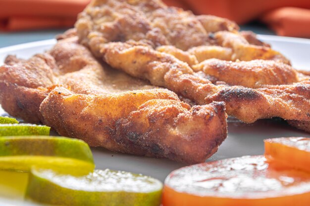 Delicioso pollo a la milanesa pollo empanado con pan rallado y huevo un plato típico brasileño En un plato blanco con tomates limón sobre mármol azul