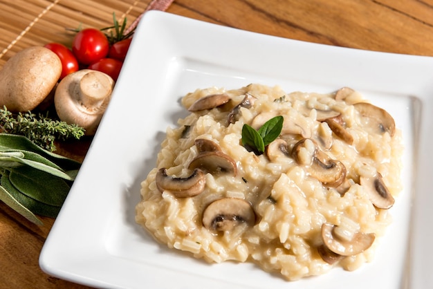 Delicioso prato de risoto de cogumelos em fundo de madeira tomate cereja e ervas em fundo preto