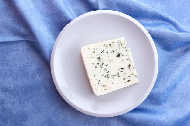 Delicioso queso azul en un plato blanco y fondo azul Primer plano de una rebanada de queso dorblu Queso azul bajo foco