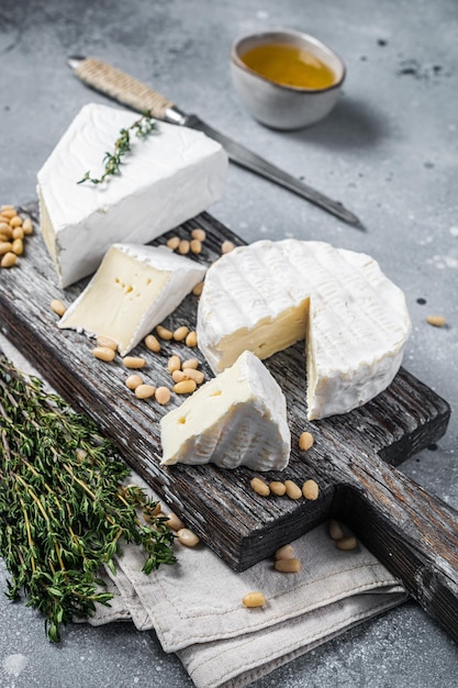 Delicioso queso brie y camembert sobre tabla de madera con hierbas y nueces Productos lácteos franceses Fondo gris Vista superior