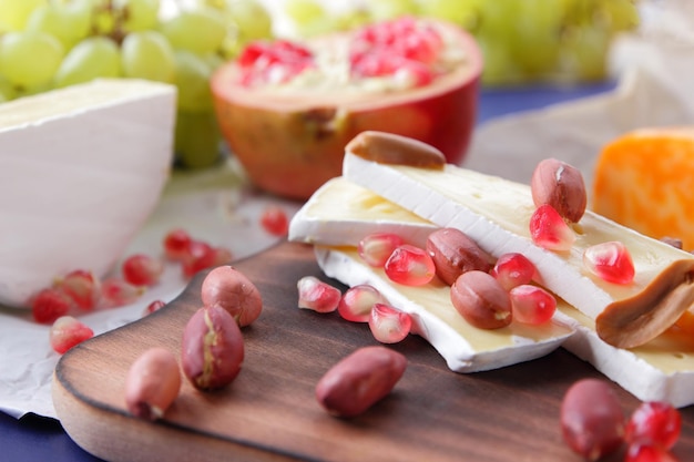 Delicioso queso sobre tabla de madera y papel pergamino de cerca Camembert con semillas de granada, uvas verdes y nueces sobre un fondo azul.