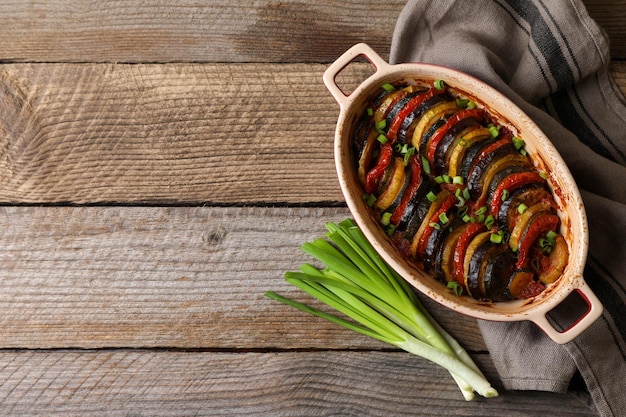 Delicioso ratatouille y cebollas verdes sobre una mesa de madera plana Espacio para texto