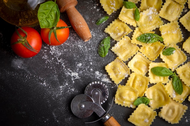 Delicioso ravioli cru com farinha e manjericão em fundo escuro. O processo de fazer ravioli italiano.